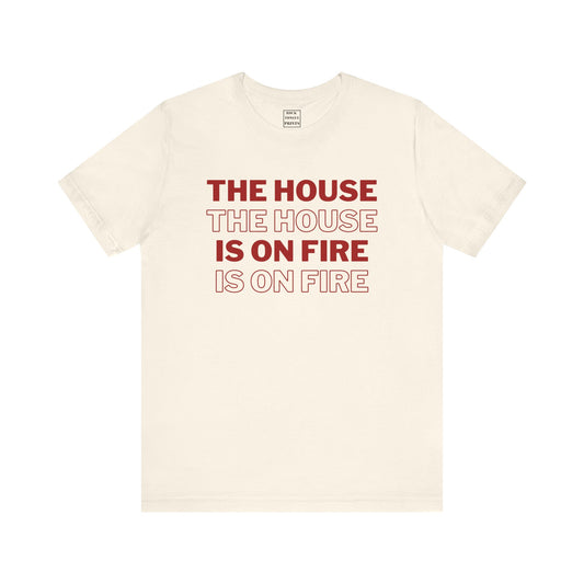 A natural colored short sleeve t-shirt with the phrase "The House is on Fire" repeated in alternating red block-color and red outline."